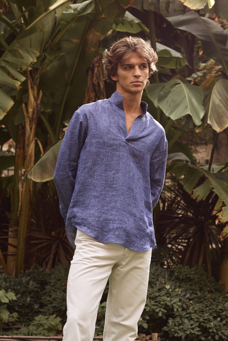 Homme dans un jardin portant une chemise en lin bleu marine à col haut, avec un pantalon blanc.