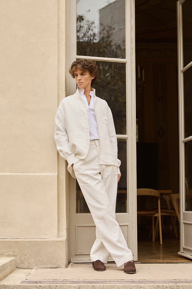 Homme adossé sur un mur, vêtu de la chemise SONGE en lin belge, de la surchemise ASTRE et du pantalon HORIZON en lin platré.