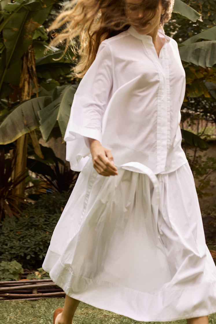 Femme courant dans un jardin portant la chemise vaporeuse en voile de coton et une longue jupe blanche en popeline de coton