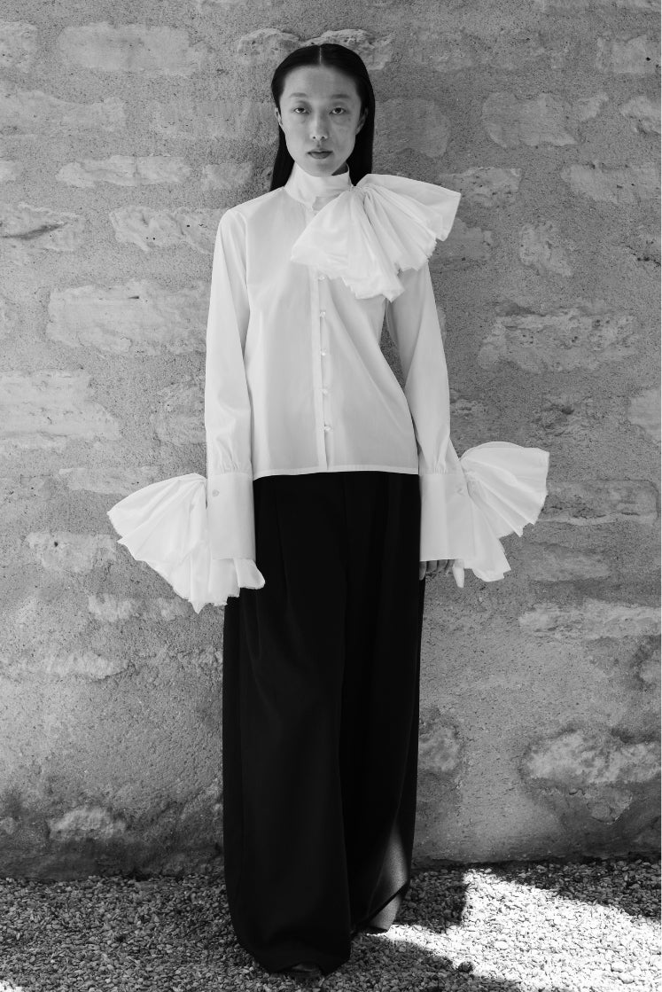 Femme portant la chemise Juliette issue de la collaboration Bourrienne Paris X et Charles de Vilmorin, avec trois fleurs en tissu attachées aux poignets et au col. 