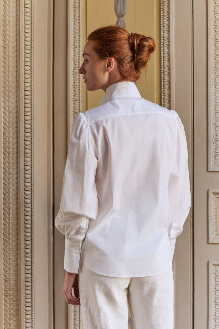 Femme portant la chemise blanche CROISIÈRE à col haut, manches légèrement bouffantes et poignets longs, vue de dos. 