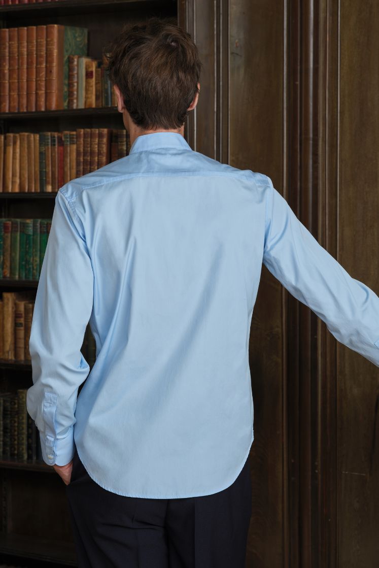 Homme de dos dans une bibliothèque portant une chemise en coton bleue, col officier, coupe ajustée. 