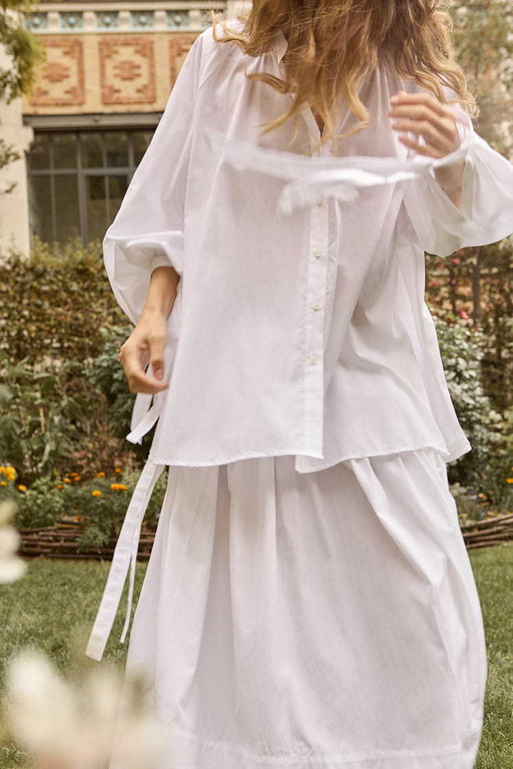 femme marchant dans un jardin portant la chemise FLIRT en coton et une jupe longue blanche