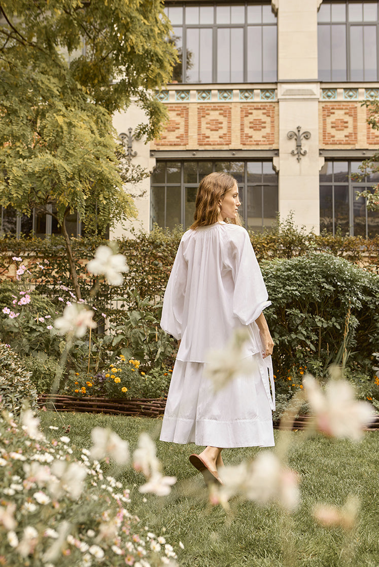 plan moyen de la mannequin portant la chemise blanche FLIRT et une jupe blanch dans un jardin