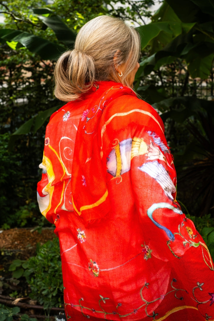 Femme de dos portant l'écharpe Fortunée en cachemire rouge dans un jardin. 