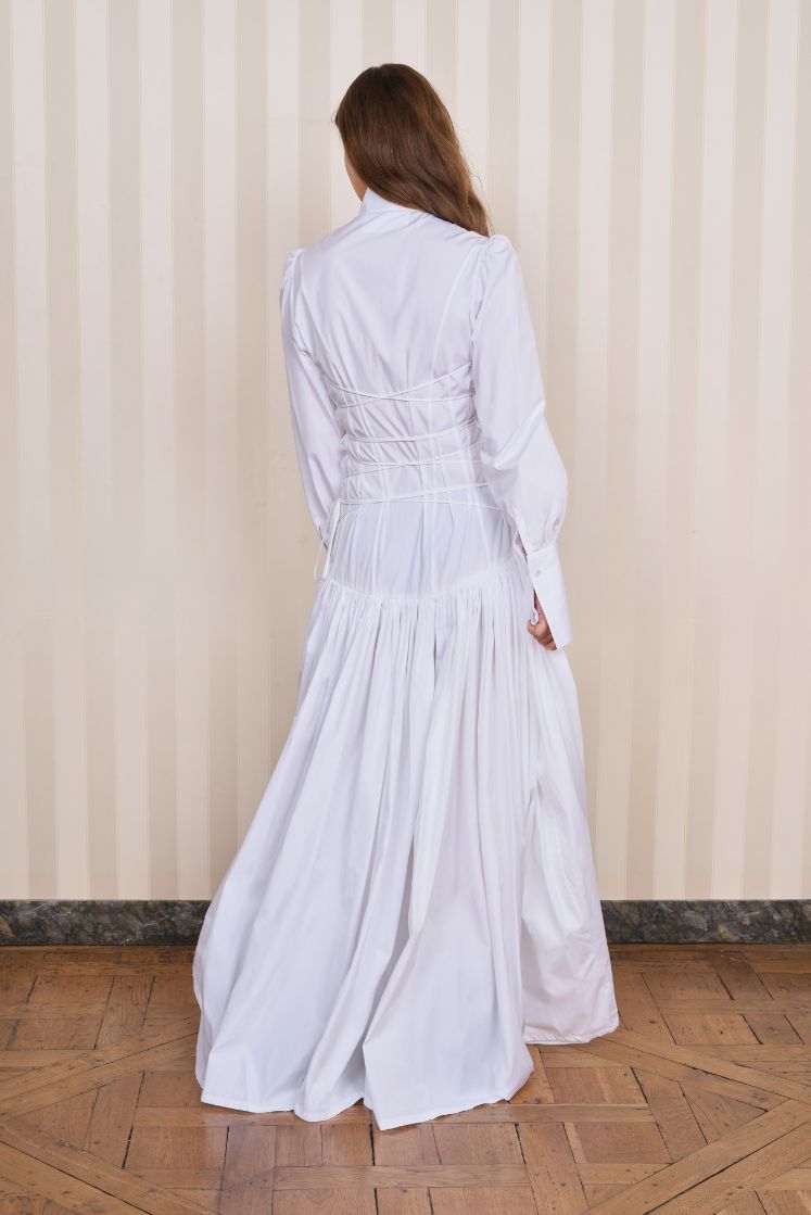Femme assise dans un canapé portant la robe-chemise longue JOSÉPHINE avec un laçage dans le dos. 