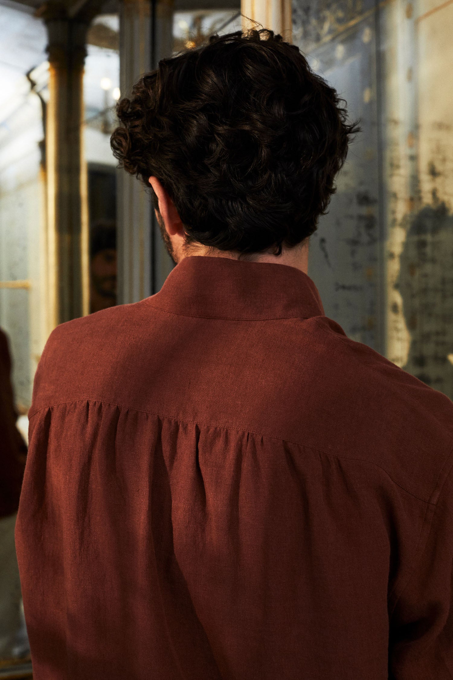 Photo d'un homme brun de dos, il porte une chemise SCULPTEUR de Bourrienne Paris X, on distingue bien les fronces dans le dos et la belle couleur terracotta. 