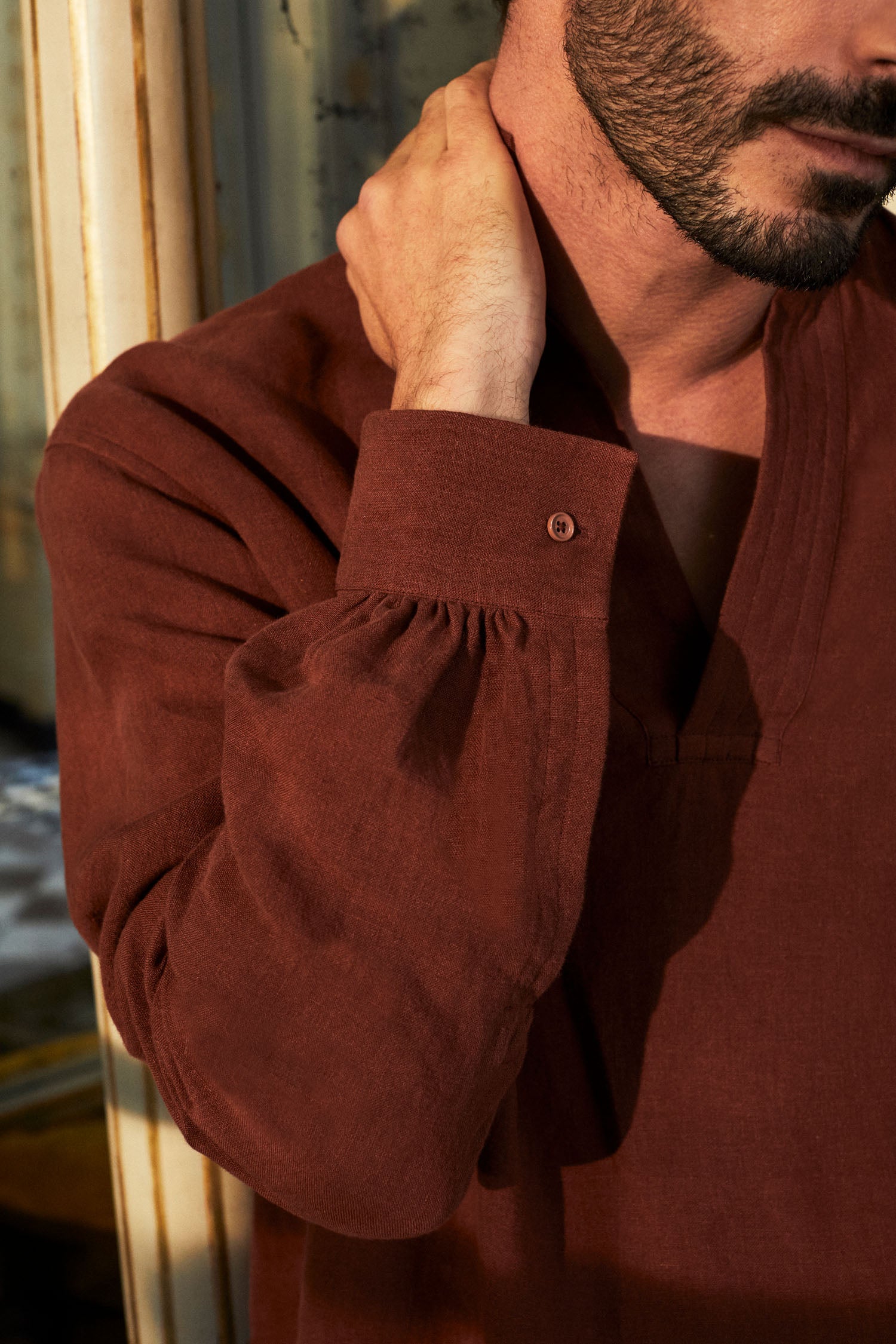 Photo plan poitrine d'un homme portant une chemise SCULPTEUR de Bourrienne Paris X en lin couleur terracotta. Il tient son cou ce qui nous laisse bien apercevoir le poignet du modèle iconique Sculpteur avec ses fronces et son boutonnage. 