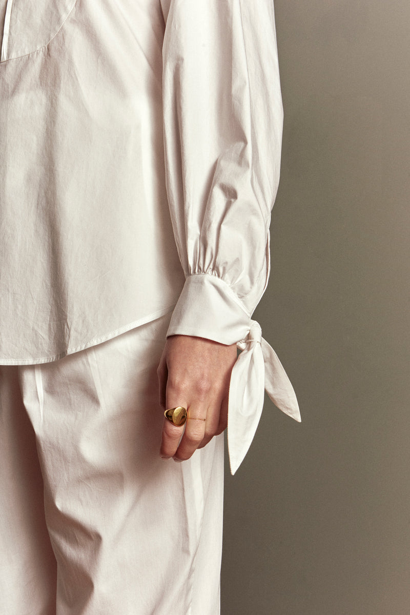 Canvas est une blouse blanche poétique, qui se noue au col et aux manches. Son plastron surpiqué signe son allure originale. Elle est coupée dans une popeline de coton lavée, qui lui donne un côté craquant.